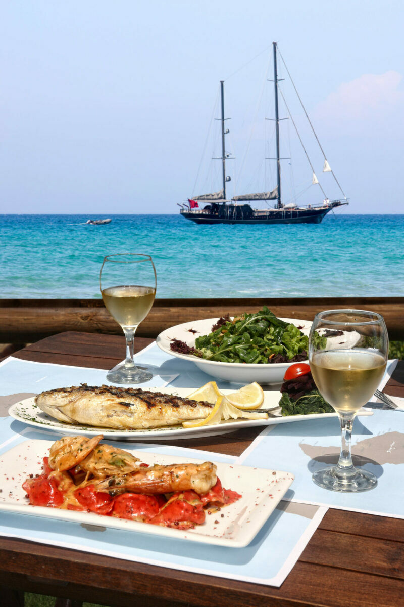 Mediterranes Essen serviert mit einem Glas Wein mit Blick auf ein Segelboot auf dem Meer