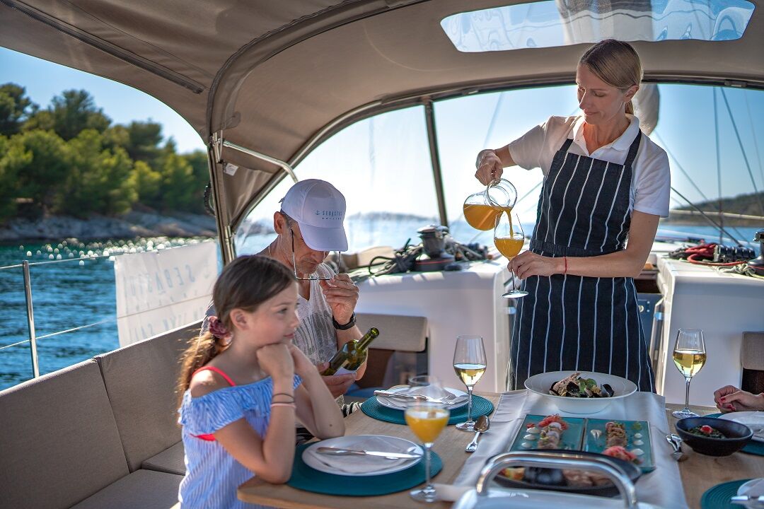 hostess serving food and drinks on a sailing boat to a family