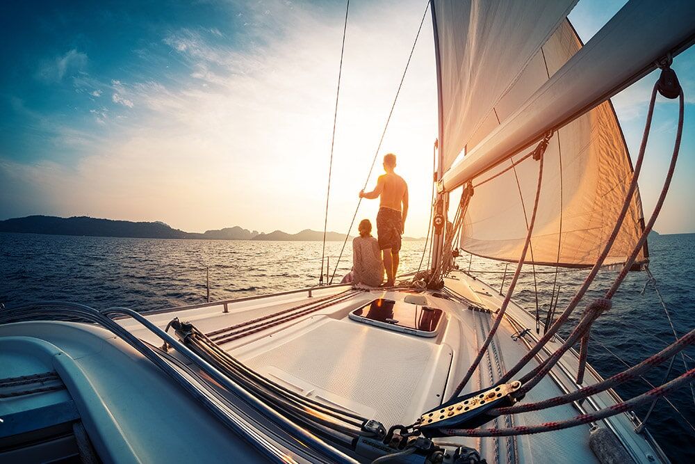 A couple looking at the sunset as they ride on their sailboat.